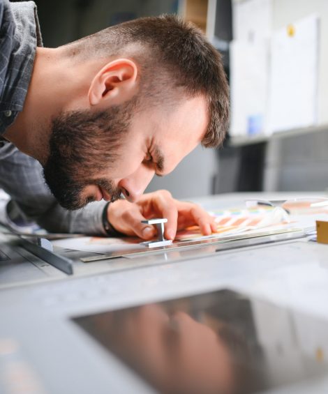 Print house worker controlling printing process quality and checking colors with magnifying glass.